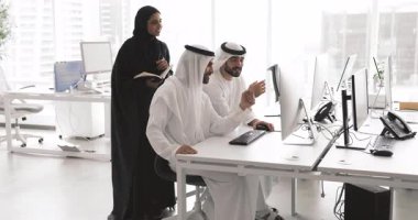 Siyah tesettüre bürünmüş Arap bir kadın kişisel organizatörüyle iki pozitif erkek takım arkadaşıyla brifingde bilgisayar başında oturmuş ortak projeyi tartışıyor. Takım çalışması, departman iş akışı