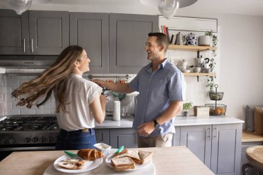 Neşeli bin yıllık evli çift modern mutfakta dans ediyor, aşk, kahkaha ve eğlence ile dolu sabahın tadını çıkarıyor, yemek masasında yeni hazırlanmış kahvaltı. Romantik randevular, kiracılık, eğlence