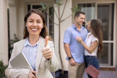 Gülümseyen emlakçı kadın kameraya bakar, başarılı bir anlaşma için olumlu bir jest yapar, en iyi emlak hizmetlerini teşvik eder, arka planda duran mutlu çifte ev satar. Satışlar kapanıyor, kira kontratı bitiyor.