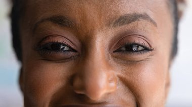 Genç, mutlu, Afro-Amerikan bir kadının gözleri kameraya bakıyor, gülümsüyor, kesilmiş makro afiş için poz veriyor. Kadın yüzü yakın plan görüş, görme ve cilt bakımını teşvik ediyor.