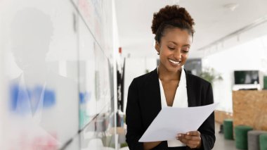 Pozitif odaklı genç Afrikalı proje lideri kadın Kanban karmaşa yönetim kurulunda finans raporu okuyor, iş planı üzerinde çalışıyor, planlama ve planlama için bilgiyi analiz ediyor. Sancak vuruşu