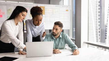 Ciddi genç Afrikalı yönetici iş planı, proje stratejisi sunuyor, iş arkadaşlarıyla konuşuyor, online sunumu dizüstü bilgisayarda gösteriyor ve açıklıyor. Çeşitli takımlar bilgisayarda birlikte çalışıyor.