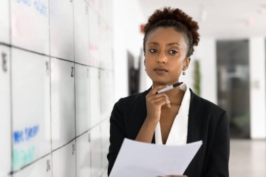 Düşünceli genç Siyahi iş projeleri yöneticisi kadın görevlendirmeyi düşünüyor, Kanban yönetim kurulunda toplantı masasını ayarlıyor, çeneye dokunuyor, başka tarafa bakıyor, kağıt tutuyordu, karar veriyor.