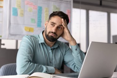 Proje çözümleri üzerine gündelik düşünen düşünceli İspanyol işadamı, dizüstü bilgisayardaki şüpheler, karar verme, kafa kafaya verme, yüzünü çevirme, dizüstü bilgisayarla çalışma masasında oturma,