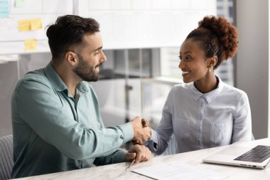 Çok ırklı iki meslektaşın müzakere, iş görüşmesi, istişare toplantısı, yardımlar, danışma ve ortaklık için birbirlerine teşekkür ederek ofis masasında el sıkışıyor.