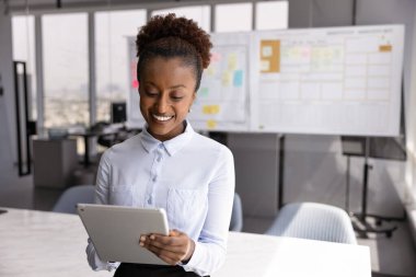 Mutlu genç Afrikalı Amerikalı iş projesi yöneticisi internet projesinde çalışıyor, sadece ofis çalışma alanında tablet bilgisayar kullanıyor, ekranda yazıyor, gülümsüyor, çevrimiçi satış artışını izliyor.