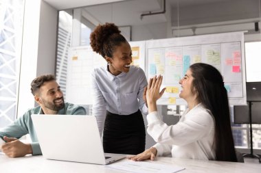 Başarılı genç, çeşitli kadın iş adamları ve proje yöneticisi ofiste yaptığı toplantıda beşlik çakarak kurumsal profesyonel başarıyı, başarıyı, takım çalışmasından keyif almayı kutluyor.