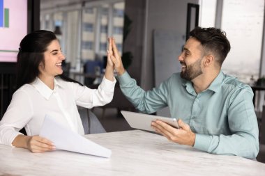 Neşeli Latin erkek ve kadın iş ortakları ofis masasında beşlik çakıyor, başarılı bir iş birliği, ortaklık, arkadaşlık, gülümseme, kahkaha