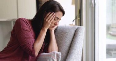 Mutsuz Latin kadın baş ağrısı çekiyor, başını tutuyor, tapınaklara dokunuyor, kanepeye oturuyor, başka yere bakıyor, sağlık sorunları yaşıyor, depresyon, hüsran yaşıyor.