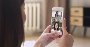 Çeşitli insanlar video konferansına katılıyor, akıllı telefon ekranı kadın omzunun üstünden görünüyor, kapatın. Aile arasında dünya çapında iletişim, kişisel haberleri paylaşın uygulamayı kullanarak arkadaşlarınızla sanal buluşmanın keyfini çıkarın
