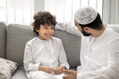 Genç Arap babasıyla oğlu arasında neşeli bir etkileşim. Geleneksel Müslüman gibi giyinmiş şirin bir çocuk. Evde koltukta oturan babasıyla keyifli sohbetler ediyor. Aile bağları, güçlü bağlar