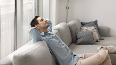 Genç İspanyol adam ellerini başının arkasına koydu modern oturma odasındaki rahat kanepeye yaslandı, hayal kuruyor, derin düşünceler kuruyor, yorgunluk gideriyor, evde stressiz bir hafta sonu geçiriyor.