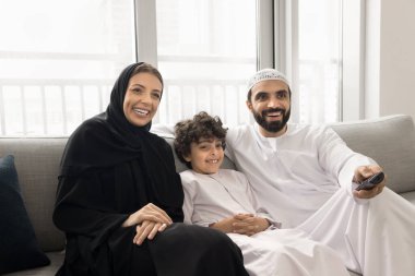 Geleneksel giyinmiş, oğlu olan Arap bir çift koltukta dinleniyor, uzaktan kumandalı kanal değiştiriyor, internetten ya da sinemadan eğitim programını seçiyor, boş zamanlarını evde geçiriyorlar.