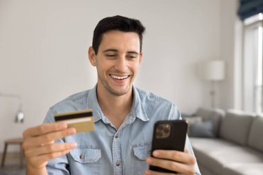 Hispanik adamın elinde kredi kartı ve cep telefonu var, pazar yeri başvurusu üzerinden satın alma, kolay, kıta uzaktan ödemeleri, fatura ödeme, para harcama, nakit ödeme, tatmin olma. E-ticaret