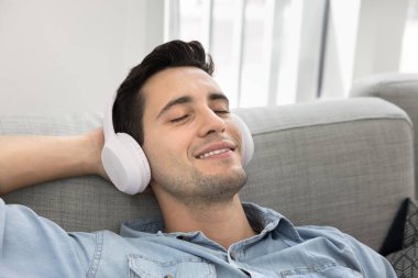 Genç adamın beyaz kulaklık taktığı, pistin tadını çıkardığı, koltuğa uzandığı, favori müziğe daldığı ya da podcast 'e daldığı rahat bir an, yakın görüş. Boş zaman, günlük rutine ara vermek.