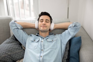 İspanyol adam rahat koltukta uzanıyor kablosuz kulaklık takıyor evde hafta sonu keyfi için favori parçalarını dinliyor dijital müzik abonelik hizmetlerini kullanıyor, hobi, dinlenme