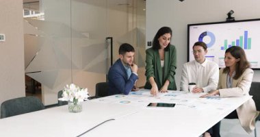 İş projesi yöneticisi kadın, toplantı masasındaki meslektaşlarına finansal strateji sunuyor, kağıt istatistik pazarlama raporlarını gösteriyor, iş arkadaşlarıyla konuşuyor, büyüme planını anlatıyor.