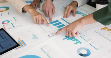 Analistlerden oluşan bir ekip, pazarlama raporlarını birlikte inceliyor, şemalara, çizelgelere, satışların büyümesi, istatistik verileri, finansal araştırmalara işaret ediyor. Vurulan takımın elleri