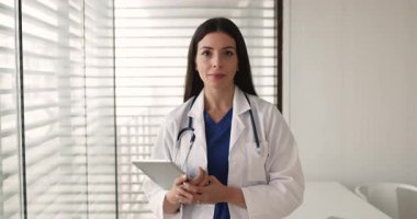 30 'ların genç terapisti ya da üniformalı kardiyolog kadının portresi elinde dijital tabletle kameraya gülümseyerek bak, modern muayene odasında tek başına dur. Görev, profesyonellik, kariyer