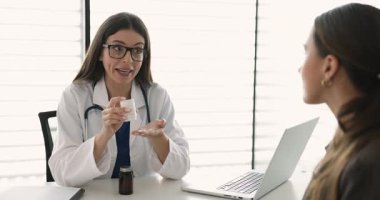 Kadın pratisyen hekim elinde ilaç şişesi, kadın hastaya ilaç talimatı veriyor, dozajı, yan etkileri, ilaçları açıklıyor. Profesyonel tıbbi danışmanlık, farmakoloji