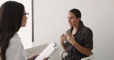 Beyaz üniformalı kadın terapist elinde dosya tutarak, kadın hastayı dikkatle dinliyor semptomları ve şikayetleri açıklıyor, sağlık endişelerini paylaşıyor. Güven, iletişim, sağlık hizmetleri