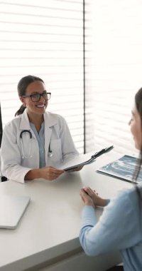 Doktor klinikteki kadın hastayla el sıkışıyor, tıbbi danışmanlık yapıyor, modern muayene odasındaki masada oturan muayeneyi sonuçlandırıyor. Güven, sağlık hizmetleri, tedavi planı onayı