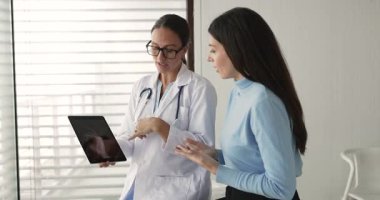 Beyaz önlüklü kadın doktor hasta kırığı, çıkığı, bağ yırtığı veya dijital tablette röntgen taramasında görülen eklem iltihabı gösteriyor, tedavi seçeneklerini ve rehabilitasyon prosedürünü açıklıyor