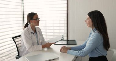 Genç kadın terapist ilaç yazıyor, etkili tedavi seçeneklerini paylaşıyor, kadın hastalarla el sıkışıyor, hastanedeki randevusunu tamamlıyor. Sağlık hizmetleri, profesyonel sağlık hizmetleri