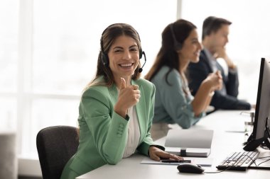 Neşeli İspanyol çağrı merkezi profesyonel kadın iş yerinde iş portresi için poz veriyor, kameraya el hareketi yapıyor, şirkette iş öneriyor, teknik destek servisi öneriyor.