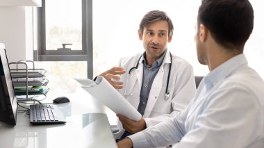 Kardiyolog, klinik müşterisiyle istişare sırasında tıbbi raporlar, test sonuçları ya da hasta kayıtları tutuyor. Pratisyen hekimler, iş yerindeki çalışma masasında bilgisayarla oturan profesyonel sağlık hizmetleri ve rehberlik sunar