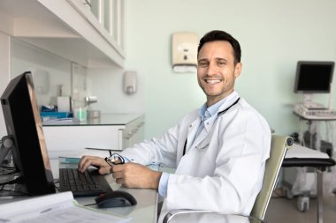 Gülümseyen profesyonel GPS 'in portresi bilgisayarla masaya oturur, kameraya bakar yaklaşan hasta danışma hazırlıklarından ve tıbbi raporlardan dikkati dağılır. Modern sağlık ve iş akışında teknoloji