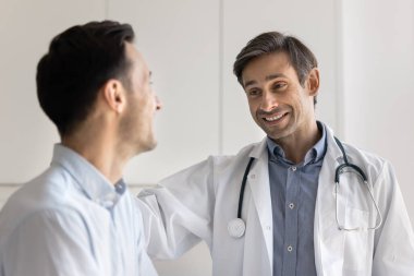 Pozitif orta yaşlı erkek kardiyolog gülümseyen erkek hastaya tavsiye ve tavsiyeler veriyor, omzuna dokunuyor, duygusal destek veriyor, dostça ilişkiler gösteriyor.