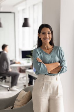 Kendine güvenen genç İspanyol iş kadını ofiste duruyor, ellerini çapraz yapıyor, kameraya bakıyor, gülümsüyor, kariyer başarısının tadını çıkarıyor, başarılı bir şirkette çalışıyor.