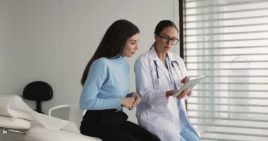 Doktor, kadın hastaya tablet üzerinde laboratuvar sonuçları veya MRI taramaları gösteriyor, teşhis açıklaması yapıyor, sağlık durumu analize dayalı, tedavi planını açıklıyor, rehabilitasyon egzersizlerini gösteriyor