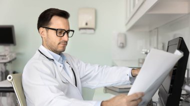 Ciddi İspanyol doktor tıbbi belgeleri veya hasta kayıtlarını dikkatlice inceliyor, laboratuvar sağlık test sonuçlarını analiz ediyor, teşhisi inceliyor, klinikte masa başında tedavi planı üzerinde çalışıyor.