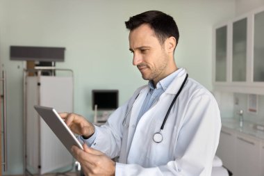 İspanyol orta yaşlı, 40 'lı yaşlarda iş yerinde tablet kullanarak çalışan, hastanın iyileşme sürecini takip eden, ilaçlarını ayarlayan, danışmanlık yapan, dijital reçeteler üreten bir pratisyen.