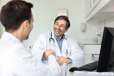 Modern tıp bürosunda dostane ve olumlu bir konuşma yapan iki doktor bilgisayar başında karşılıklı saygı göstererek el sıkışıyorlar. Takım çalışması, başarılı tartışmanın sonucu