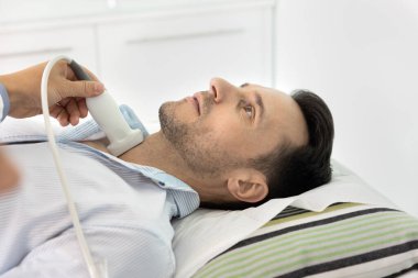 Ultrason tarama işlemi sırasında muayene masasında yatan adama yakın durun. Bilinmeyen sonograf doktoru hastanın boynuna sonda uyguluyor, hastanın boğazını, lenf düğümlerini, tiroid hastalığı için inceliyor.