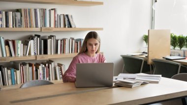 Yemek yemek. Kendine güveni tam genç bir kız öğrenci kampüs kütüphanesinde oturuyor kağıt kitaptan gelen bilgileri kontrol ediyor ödev makalesi hazırlıyor bilimsel araştırmalar yapıyor.