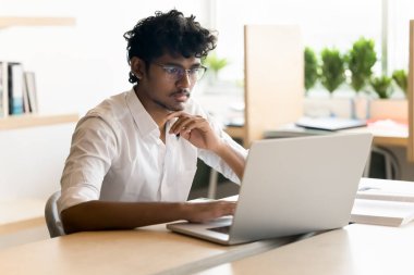 Uzak çalışma ya da öğrenme. Gözlük öğrencisi girişimci odaklı genç adam ofis masasında oturur dizayn kodlaması için not defteri kullanır e-posta sörfü bilgisi yazıp proje raporu hazırlar