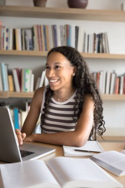 Yüksek kalite. Mutlu, genç bayan öğrenci, kütüphanede uzak öğrenim için bilgisayarını kullanıyor. Tezahüratlı bir gülümsemeyle ekranın üstüne bakıyor. Sınav sonuçlarından memnun.