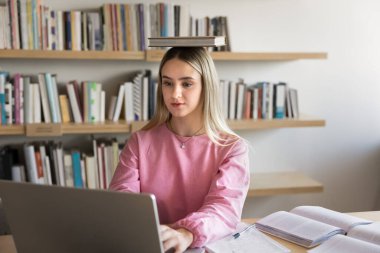Vücut ve zihin çalışıyor. Güzel kız öğrenci sınıfın masasında oturup edebiyat ödevi tezi üzerine çalışıyor. Elinde düz duruş için kağıt kitap tutuyor.