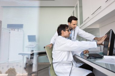 Üniforma giymiş iki odaklanmış Latin erkek doktor hasta için tedavi seçeneklerini tartışıyor bilgisayar kullanıyor, tıbbi laboratuvar sonuçlarını araştırıyor, taramaları yorumluyor, durumu gözden geçiriyor ya da teşhis koyuyor.