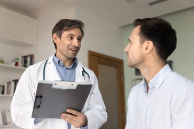 Adam kardiyolog pano tutuyor, hastayla dostane bir konuşma yapıyor. Doktorun tanısal görüşleri, sağlık tavsiyeleri, hastane randevusu sırasında tedavi seçenekleri hakkında konuşmasını dinliyor.