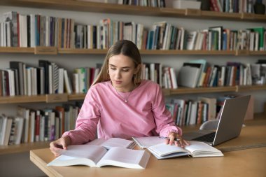 Çalışkan bir öğrenci. Sınıf veya kütüphanede uzak öğrenim öz eğitim oturumunda olan meşgul bir kadın kağıt edebiyatı okur. İnternette bilgi taramak için not defteri kullanın. Elle not alın.