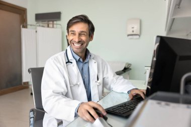 Gülen terapist masada oturup bilgisayar üzerinde çalışıyor. Profesyonel tıp çalışanı klinikteki verimli iş akışından memnun ya da gurur duyuyor, iyimserlik yayıyor, başarıların tadını çıkarıyor ya da ara veriyor.