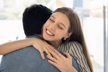 Uzun bir ayrılıktan sonra sevgilisine sıkıca sarılan, onu özleyen, samimi gülümsemesi ve gözleri kapalı derin sevgi ve mutluluğu ifade eden neşeli genç kadının yüzünü kapat. İlişki, aşk