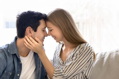 Yakın oturan genç çiftin yakın çekim görüntüsü gülümsemeleri ve gözleri kapalı alınlarına dokunmak derin duygusal bağlarını, sevgisini ve samimiyetini ifade eder. Romantik ilişkiler, aşk ilanı