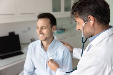 Stetoskop kullanan beyaz önlüklü doktor kalp atışlarını dinliyor, klinikteki muayenehane ziyareti sırasında göğsüne fonendoskop yerleştiriyor. İlaç ve kalp hastalıklarının önlenmesi 40 'lardan sonra