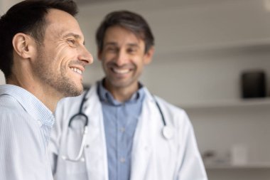 Pozitif sağlık deneyimi, güven, sigorta. Yakından, gülümseyen hasta neşeli bir ifadeyle mesafeye bakar, etkili bir tedavi ile iyimserlik ve tatmin yayar, arka plandaki doktor